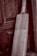 A wooden cricket bat leaning against an aged, textured wooden door. The bat has a light wooden color and visible grain patterns, with a taped handle. The background features a rich, dark wood with intricate panels and a slightly weathered appearance.