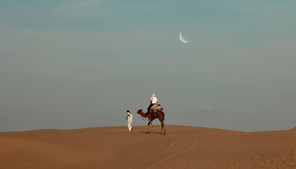 man in white shirt riding camel on brown sand during daytime