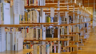 Rows of wooden bookshelves filled with books, many of which have Asian scripts on their spines, create an organized and serene library environment. The shelves are aligned in parallel, providing a sense of depth and repetition.