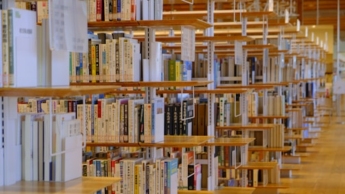Rows of wooden bookshelves filled with books, many of which have Asian scripts on their spines, create an organized and serene library environment. The shelves are aligned in parallel, providing a sense of depth and repetition.
