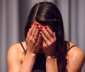 woman in black tank top covering her face with her hands