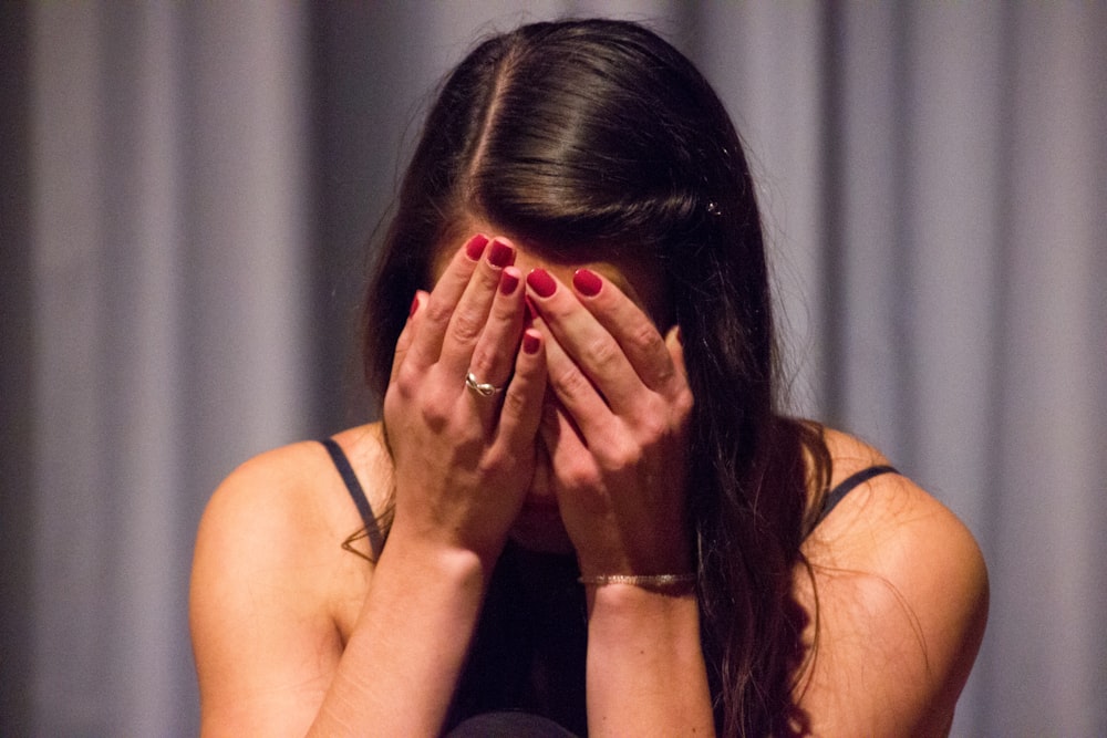 woman in black tank top covering her face with her hands