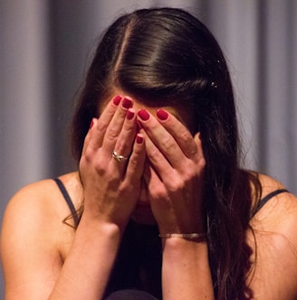 woman in black tank top covering her face with her hands