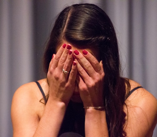 woman in black tank top covering her face with her hands