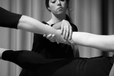 A close-up black and white photograph of three people interacting. One person appears to be holding the arm of another individual, while a third arm extends in the scene. The focus is on the hands and arms, creating a sense of connection and support.