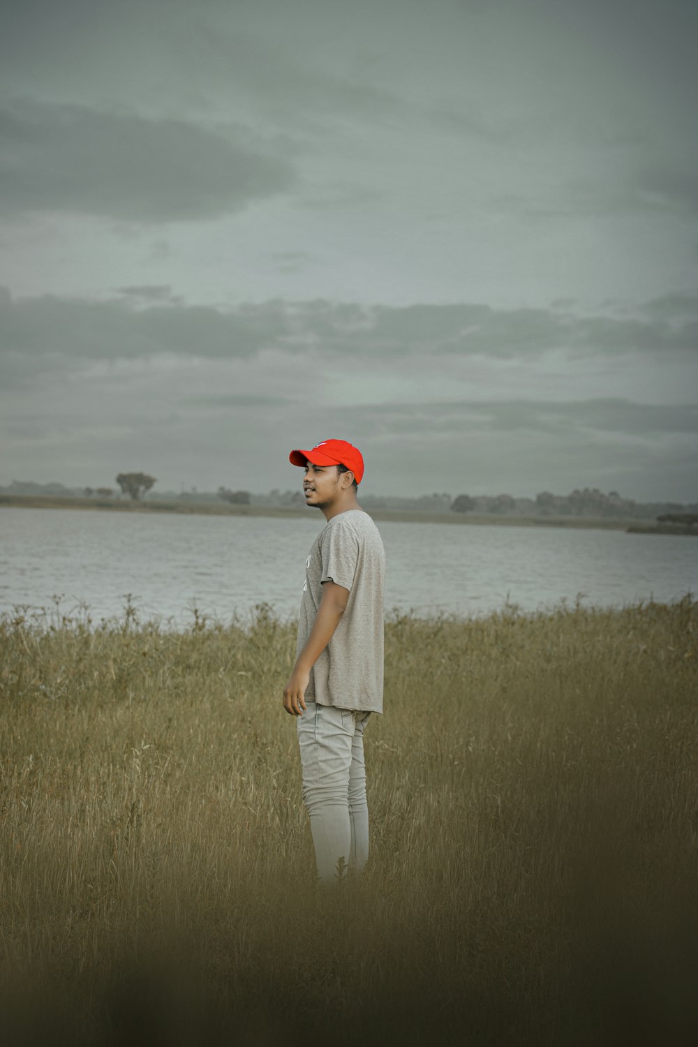 man in white t-shirt and white pants standing on green grass field near body of on with on with