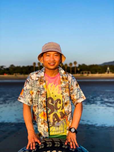 A vibrant Hawaiian-themed t-shirt and matching hat laid out on a lava rock with tropical flowers nearby.