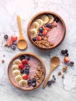 Two acai bowls with banana slices, berries, and granola in wooden bowls