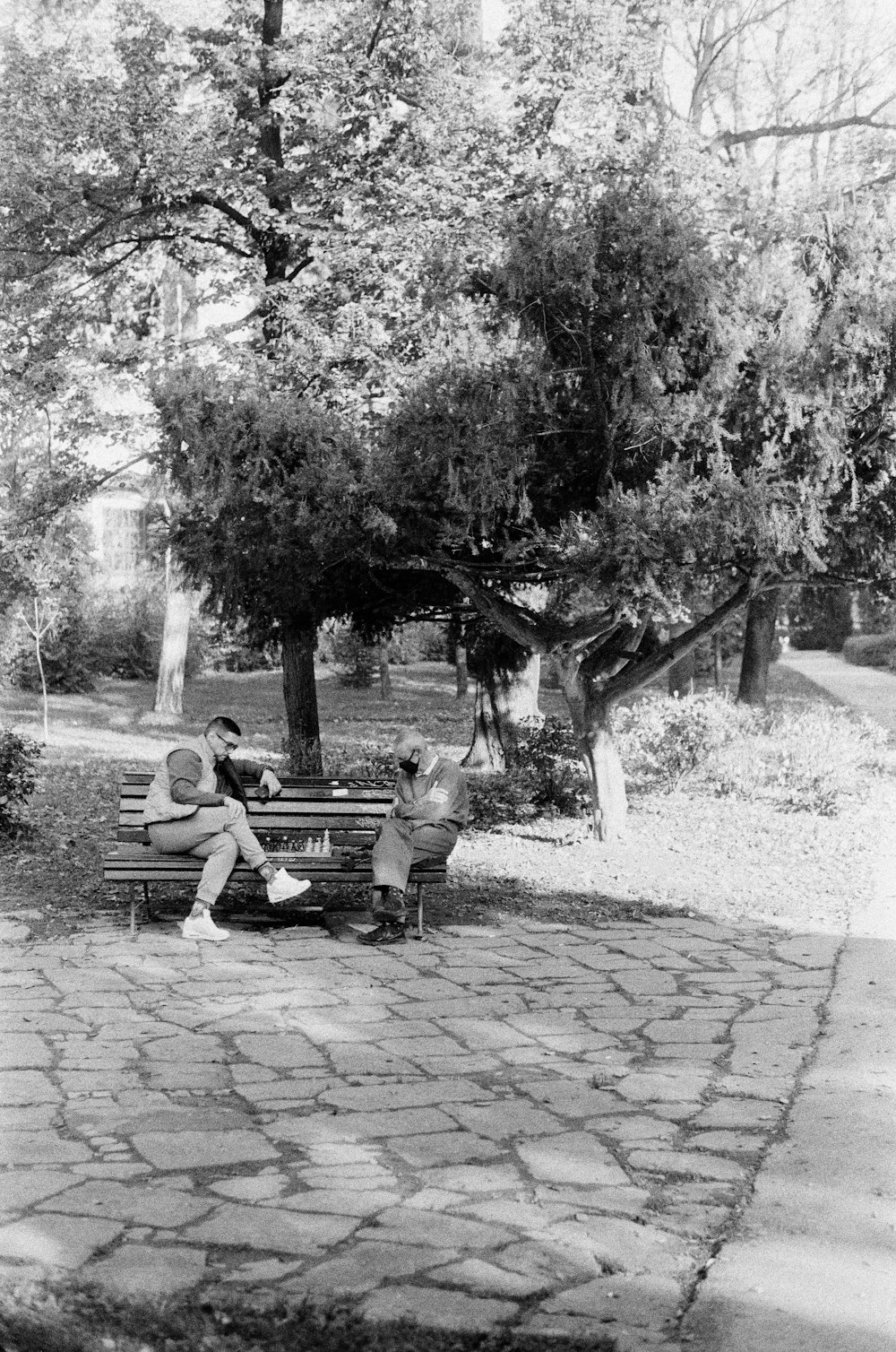 grayscale photo of 2 men sitting on bench near trees