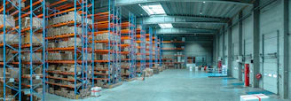 Tall blue metal shelving units filled with cardboard boxes in a large warehouse