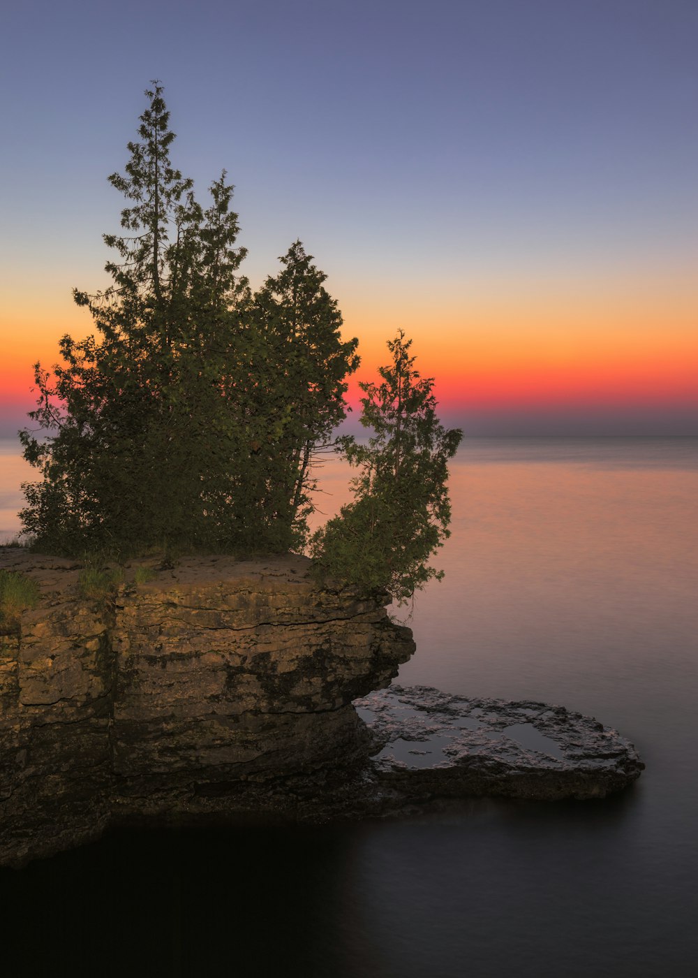 Arbre vert sur une formation rocheuse près du plan d’eau au coucher du soleil