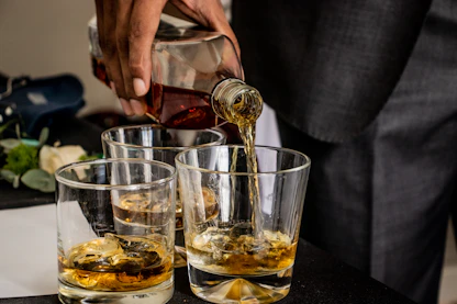 person pouring bourbon on clear drinking glass