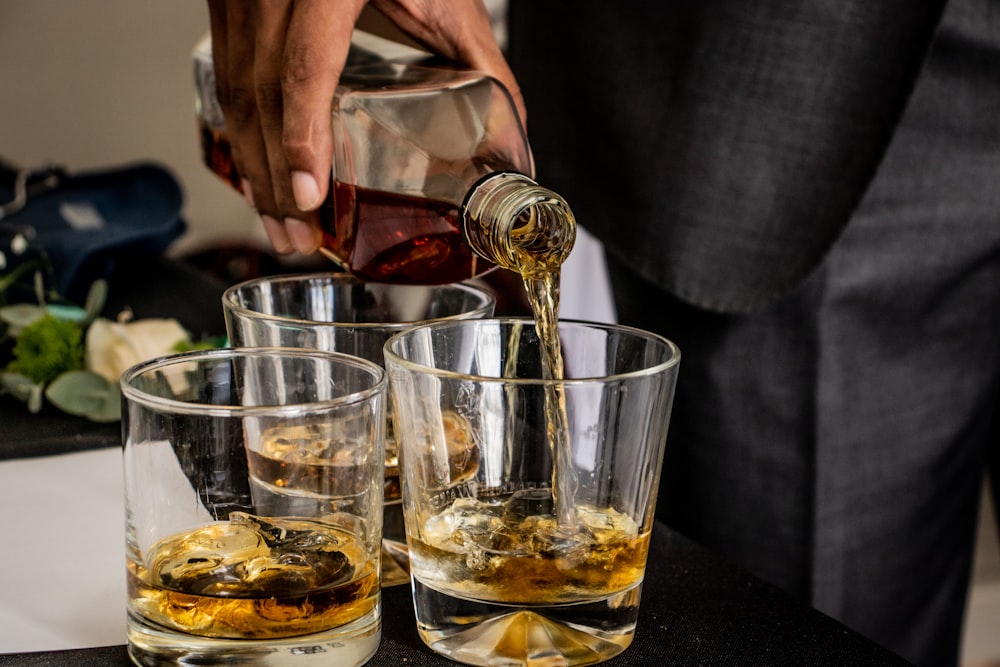 person pouring brown liquid on clear drinking glass