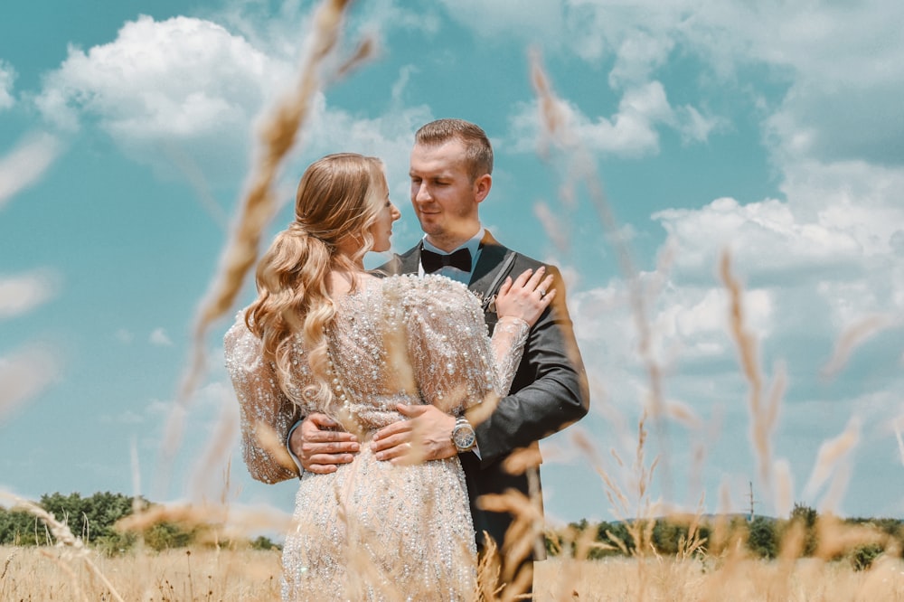 man in black suit jacket kissing woman in white floral lace dress on brown grass field