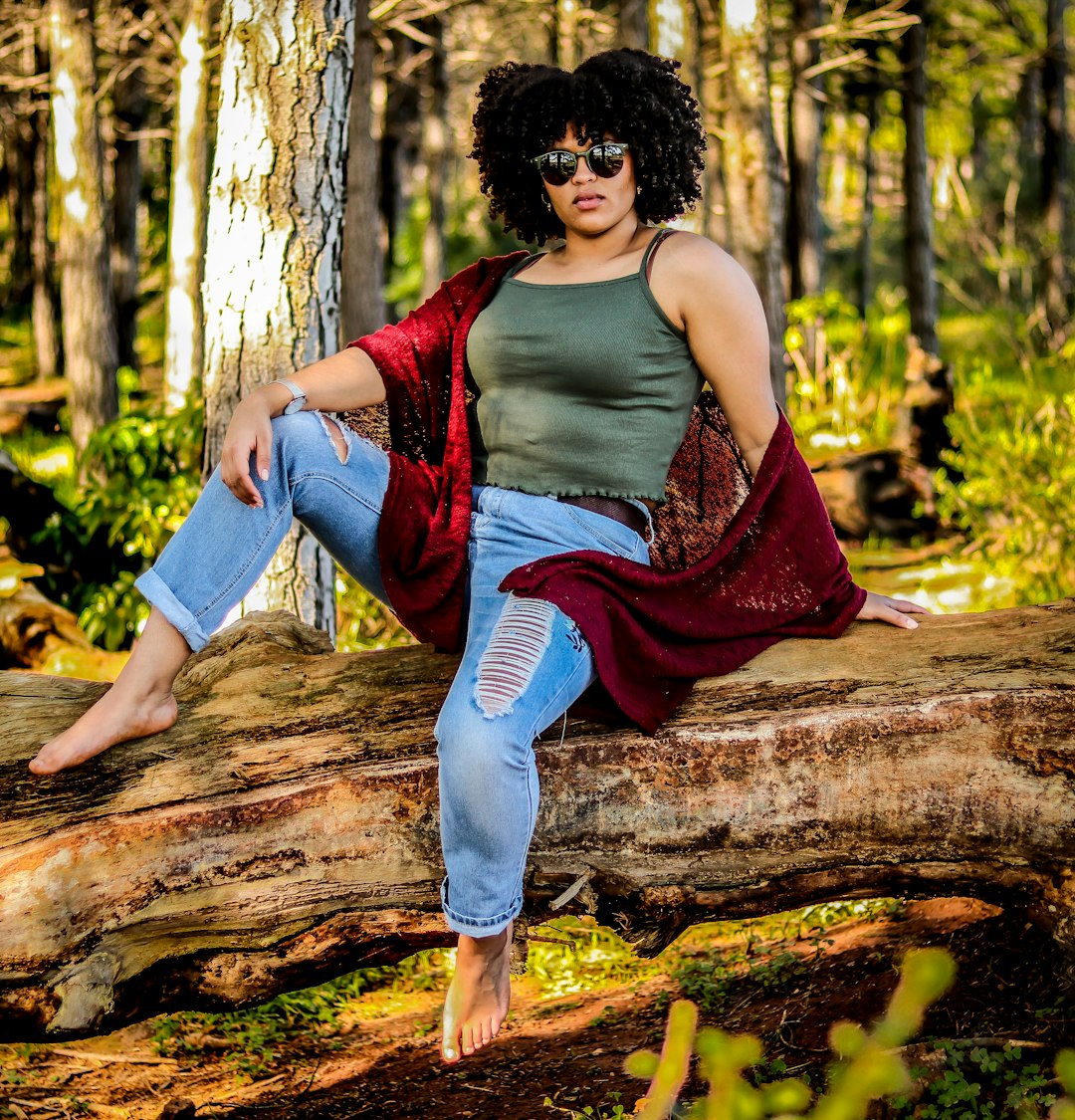 woman in purple tank top and blue denim jeans sitting on brown tree log