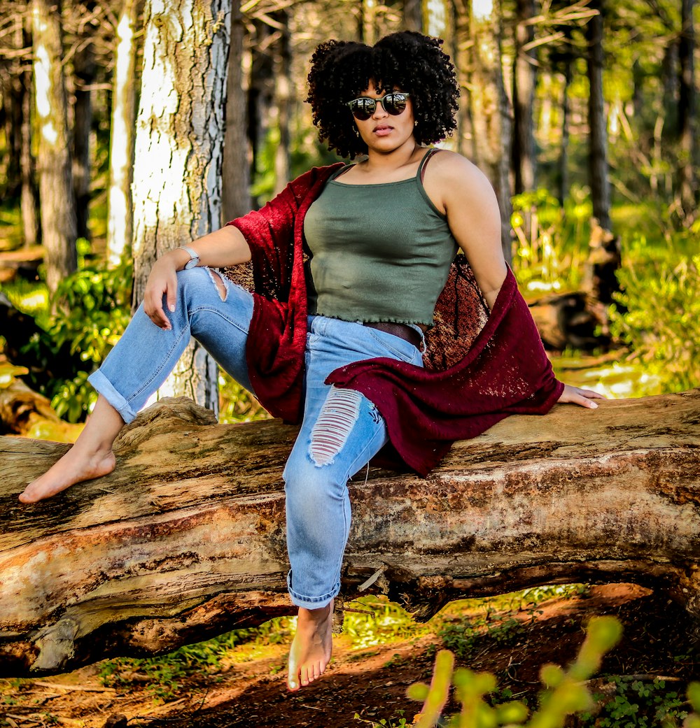 woman in purple tank top and blue denim jeans sitting on brown tree log