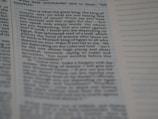 A close-up of a book page with printed text on it. The left side contains a passage from a book with a visible paragraph structure. On the right side, there is a section with lined space for notes. The text is dense and seems to be part of a narrative or dialogue.