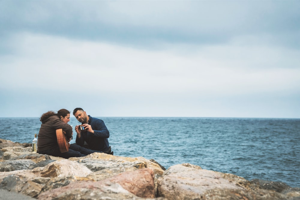 man and woman sitting on rock near sea during daytime