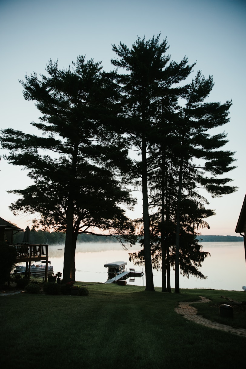 Peaceful lakefront property at sunrise with backyard dock and boat on still water.