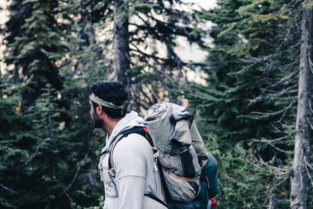 man in gray jacket wearing black cap and backpack standing in forest during daytime