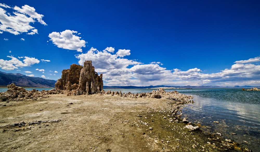 brown rock formation on sea shore under blue sky and white clouds during daytime