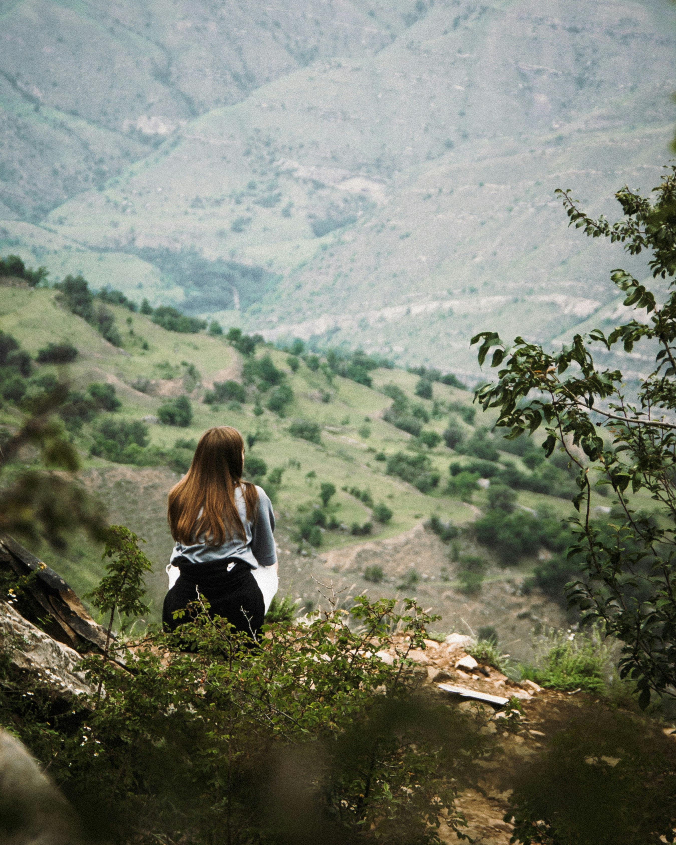 woman in white long sleeve shirt and black pants sitting on brown rock during daytime