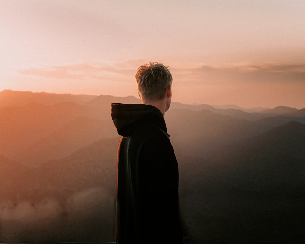 man in black coat standing on top of mountain during sunset