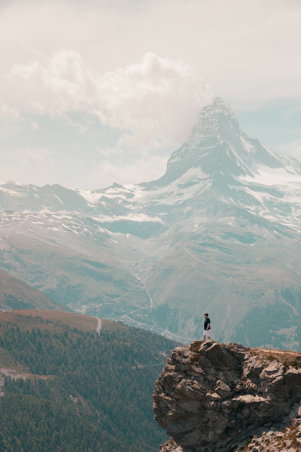 personne debout sur un rocher près d’une montagne enneigée pendant la journée