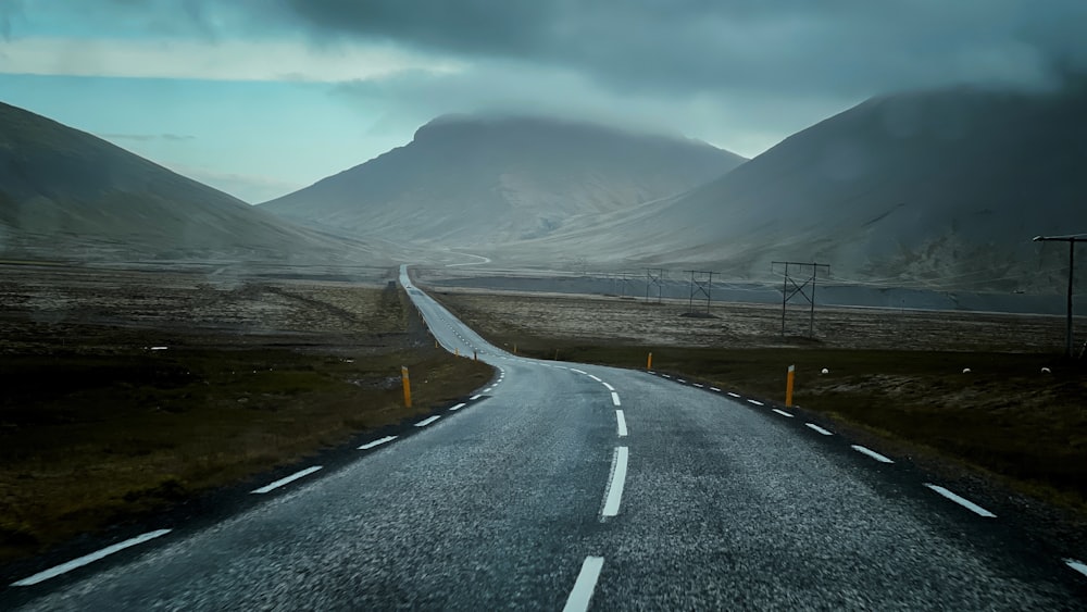 gray concrete road near mountain under white clouds during daytime