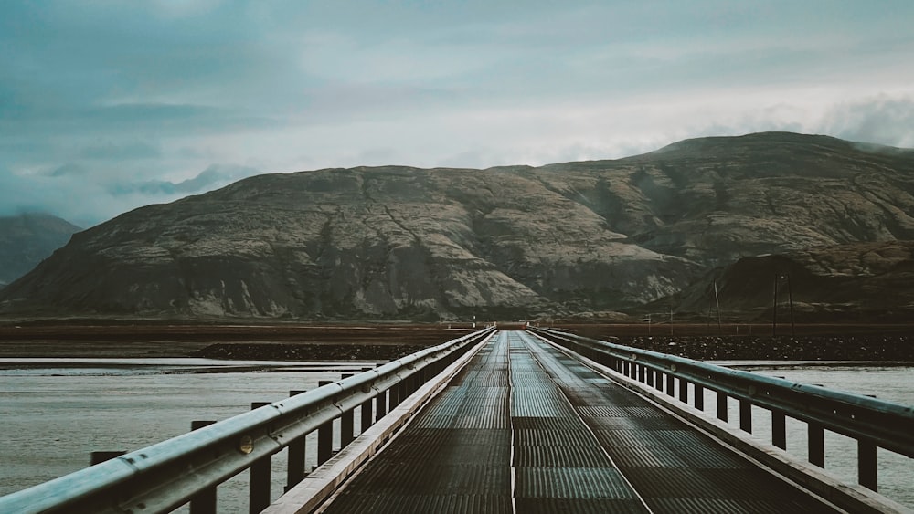 gray metal train rail near body of water and mountain during daytime