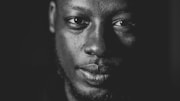 A close-up monochrome portrait of a man's face, highlighting strong contrasts and textures with dramatic lighting that emphasizes facial features.