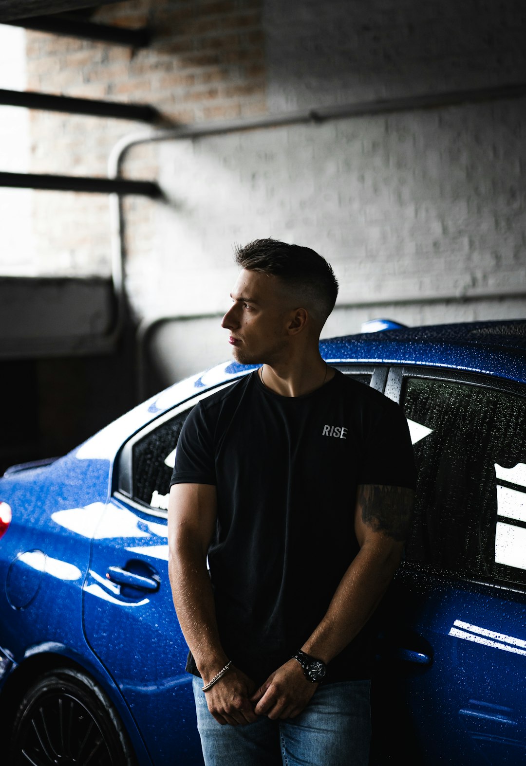 man in black crew neck t-shirt standing beside blue car