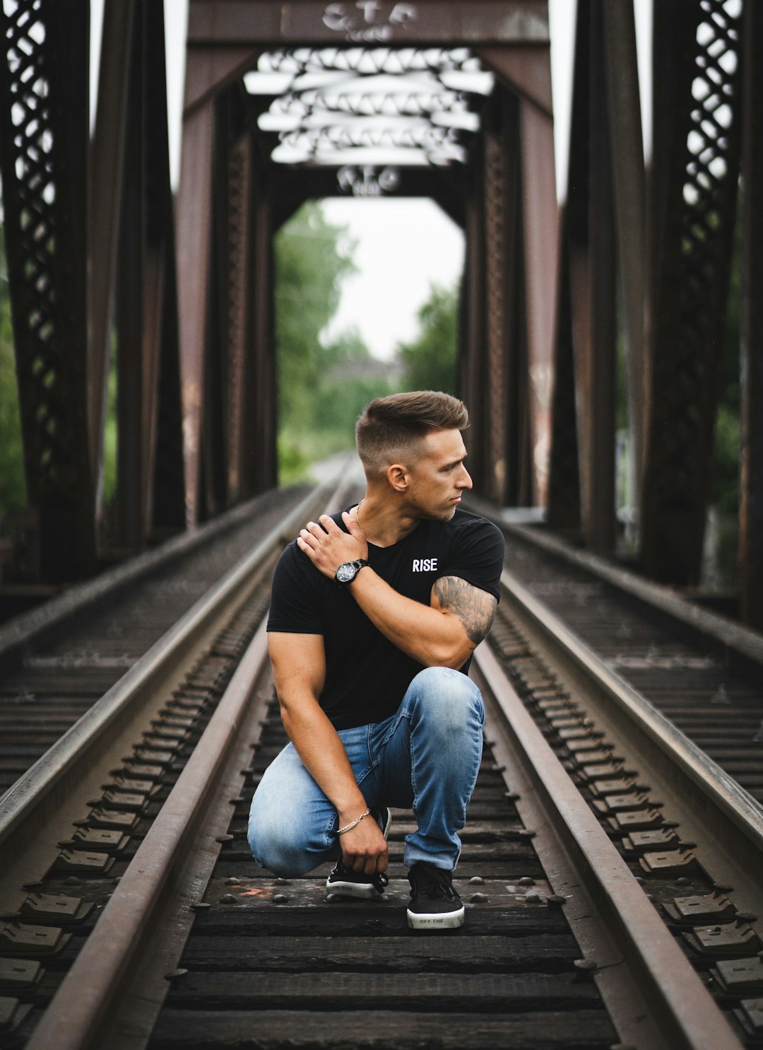man in black crew neck t-shirt and blue denim jeans sitting on train rail during