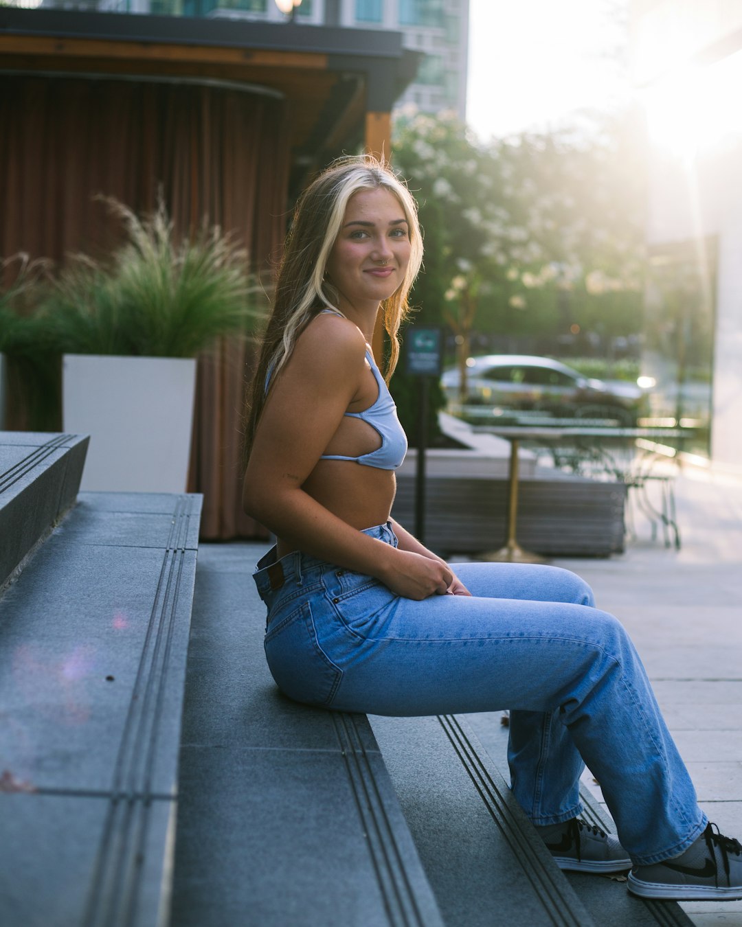 woman in white tank top and blue denim jeans sitting on gray wooden bench