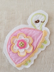 A colorful embroidered patch featuring a stylized turtle design with a pink shell adorned with layered fabric petals. A decorative button is placed at the center of the petals. The background is a textured, light-colored fabric.