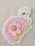 A colorful embroidered patch featuring a stylized turtle design with a pink shell adorned with layered fabric petals. A decorative button is placed at the center of the petals. The background is a textured, light-colored fabric.