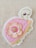 A colorful embroidered patch featuring a stylized turtle design with a pink shell adorned with layered fabric petals. A decorative button is placed at the center of the petals. The background is a textured, light-colored fabric.