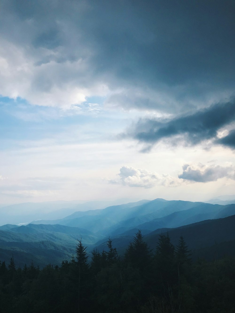 green trees and mountains under white clouds and blue sky during daytime