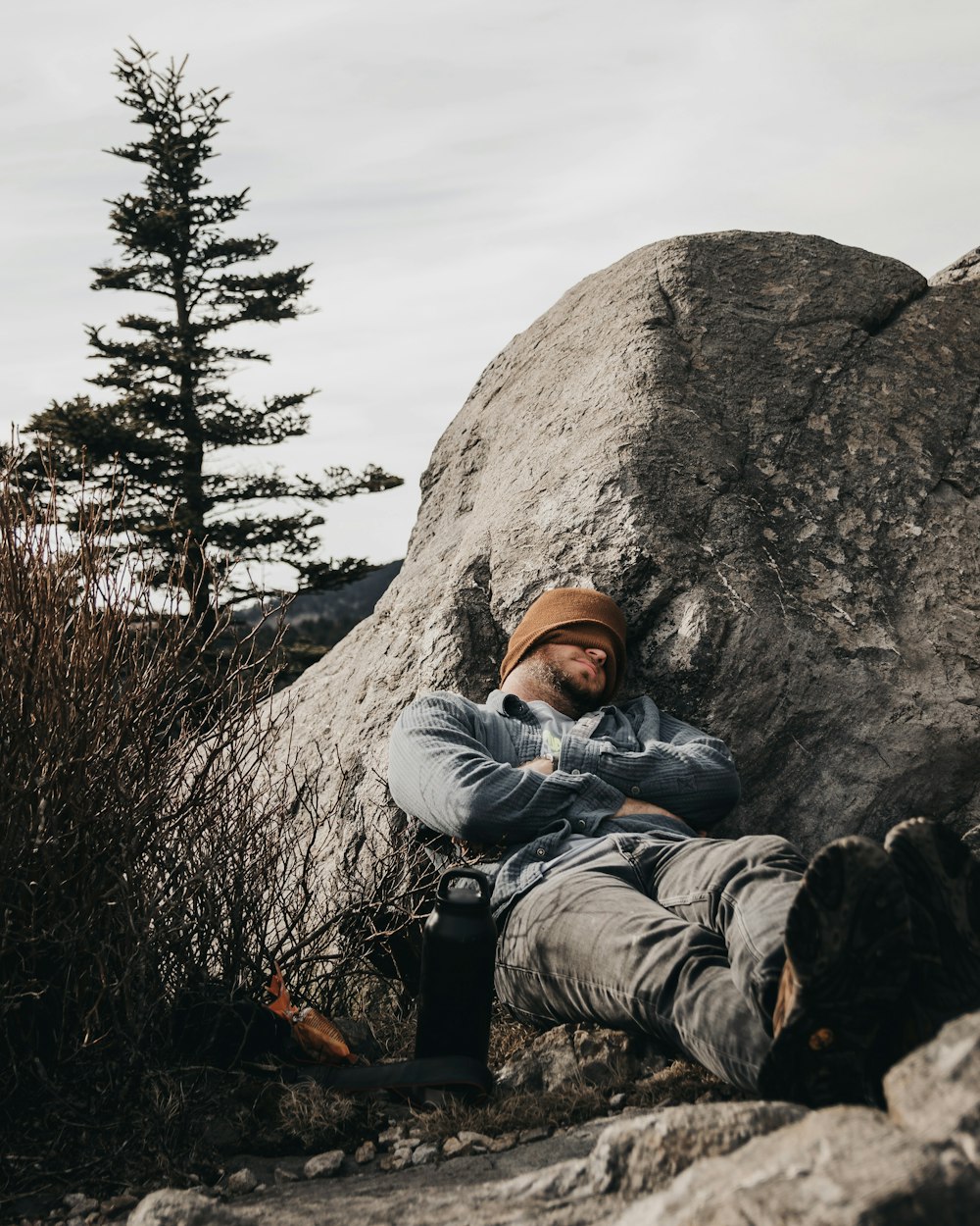 Homme en sweat à capuche gris et chapeau marron assis sur la roche grise pendant la journée