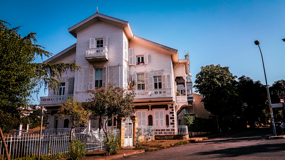 Two-story white house with balcony, surrounded by trees on a street corner at dusk