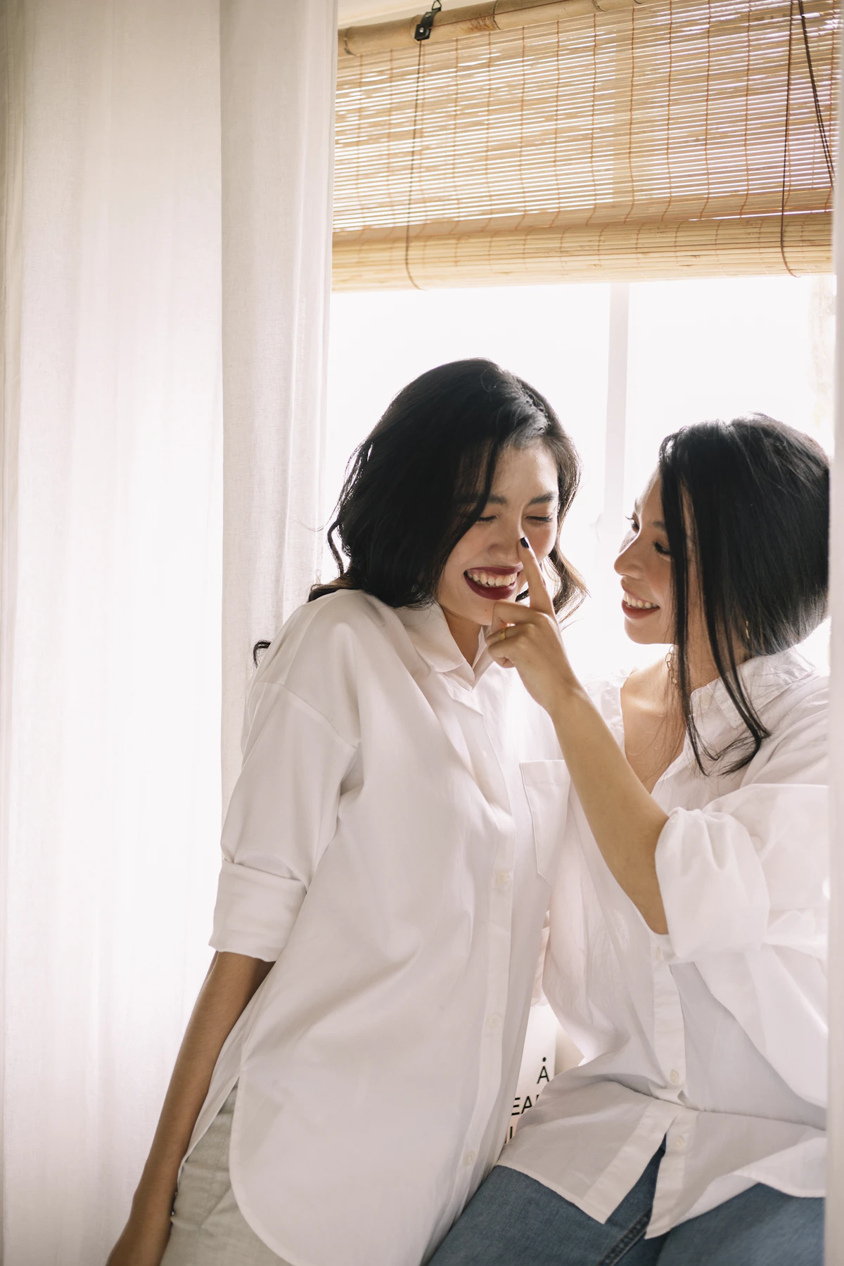 Two women in white shirts laughing together in bright, warm light
