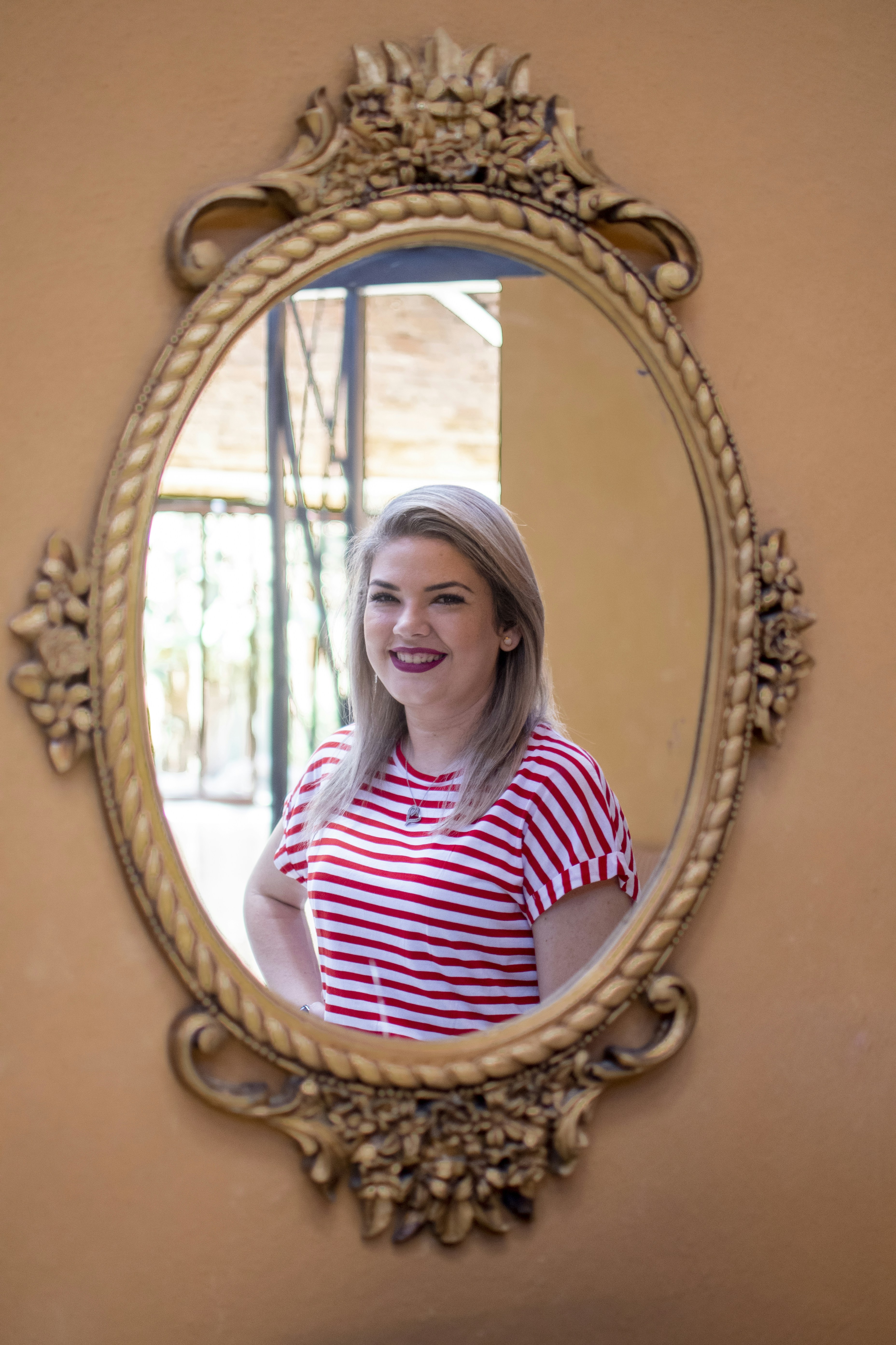 woman in red and white striped shirt standing in front of brown wooden framed mirror