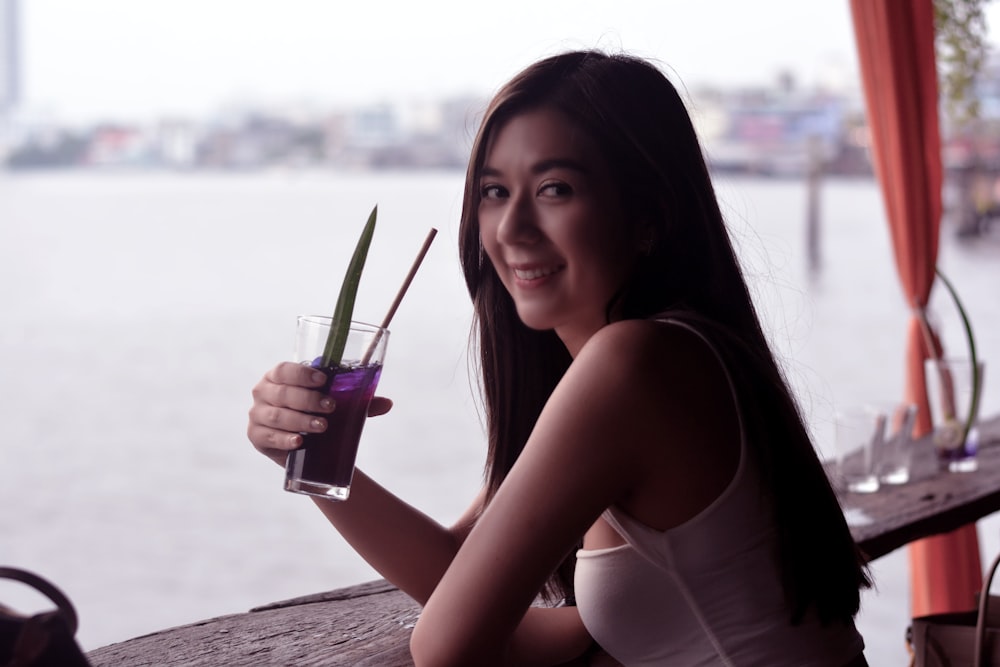 woman in white tank top holding glass cup