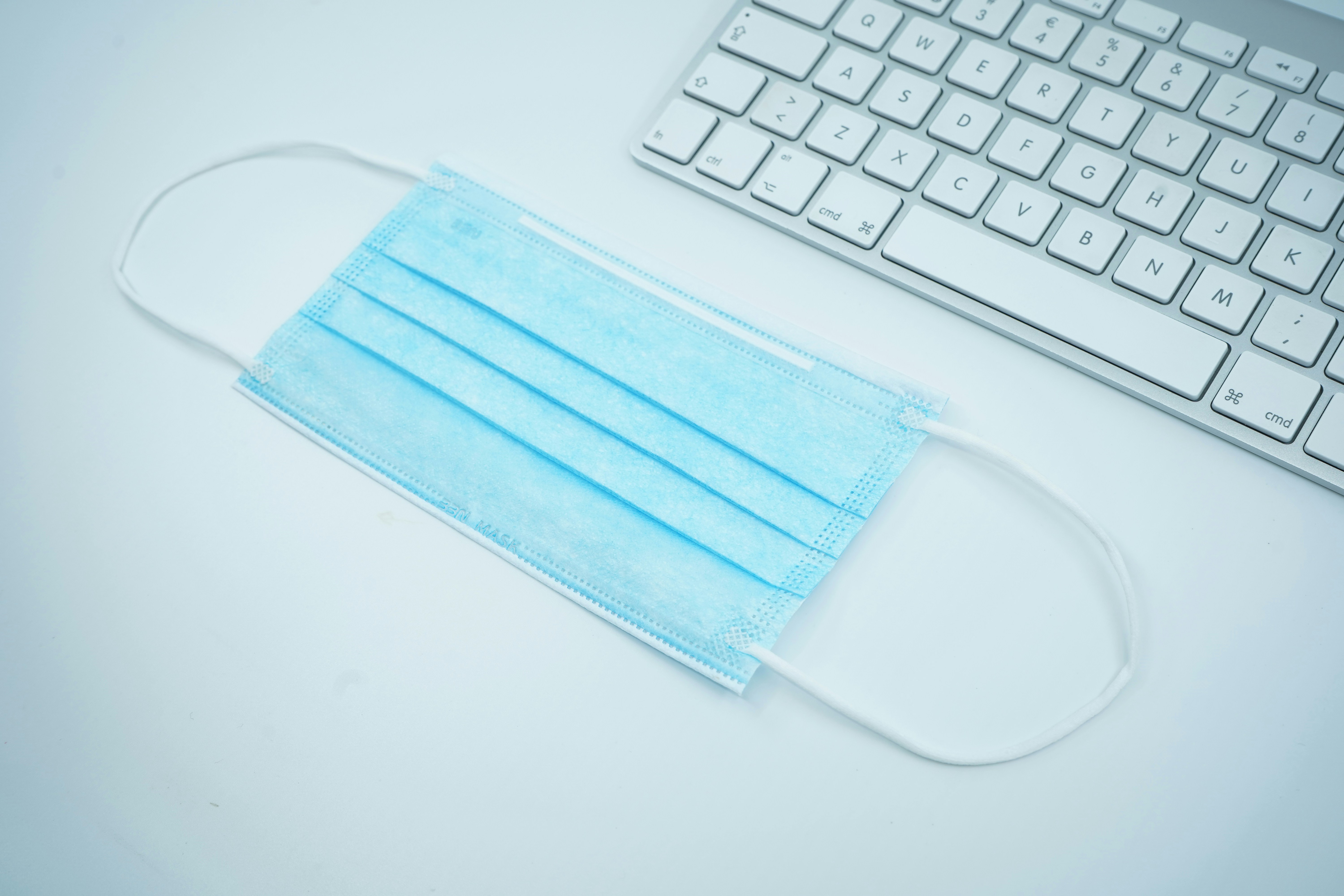 A facemask lying in front of a computer keyboard. The photo symbolizes remote and online work during covid-19 lockdown.