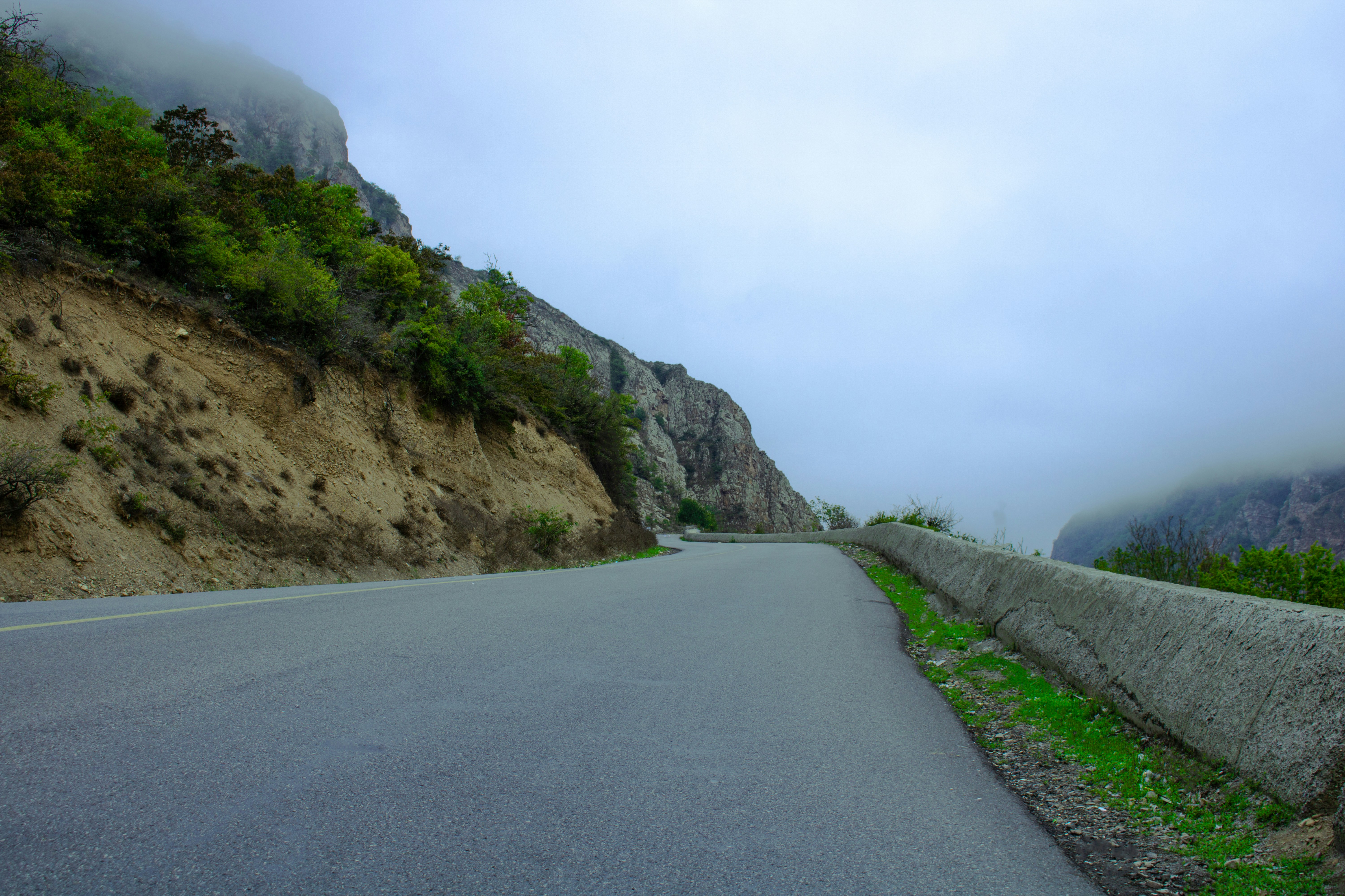 gray concrete road between green grass and brown rocky mountain during daytime