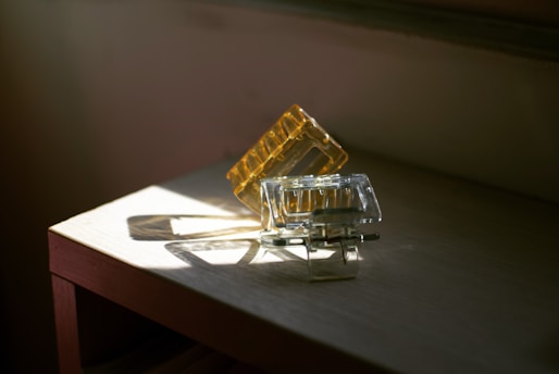 A pair of translucent hair clips, one amber and one clear, rest on a wooden surface. They are illuminated by natural light coming through a nearby window, casting soft shadows on the table.