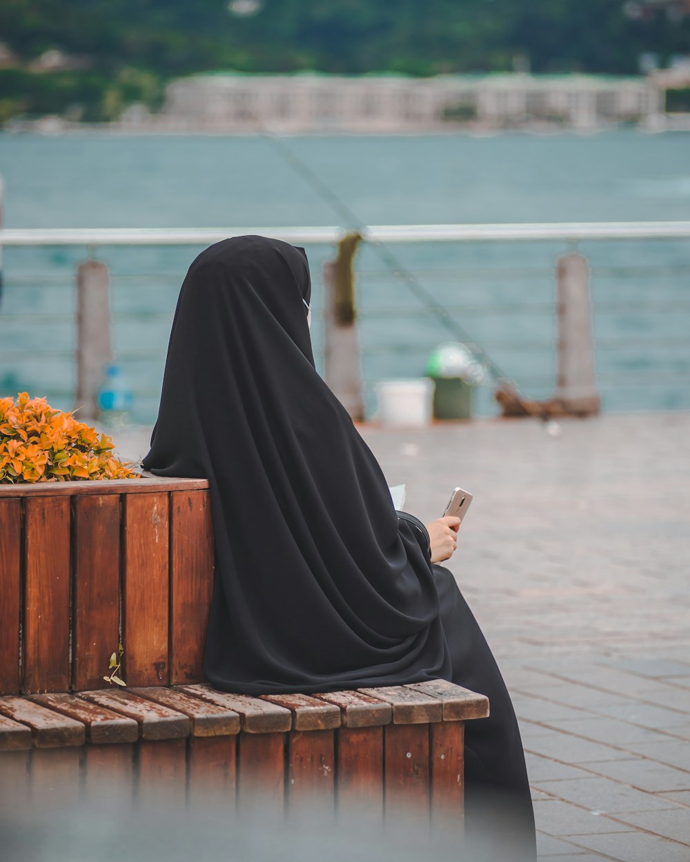 Femme en hijab noir assise sur un banc en bois brun