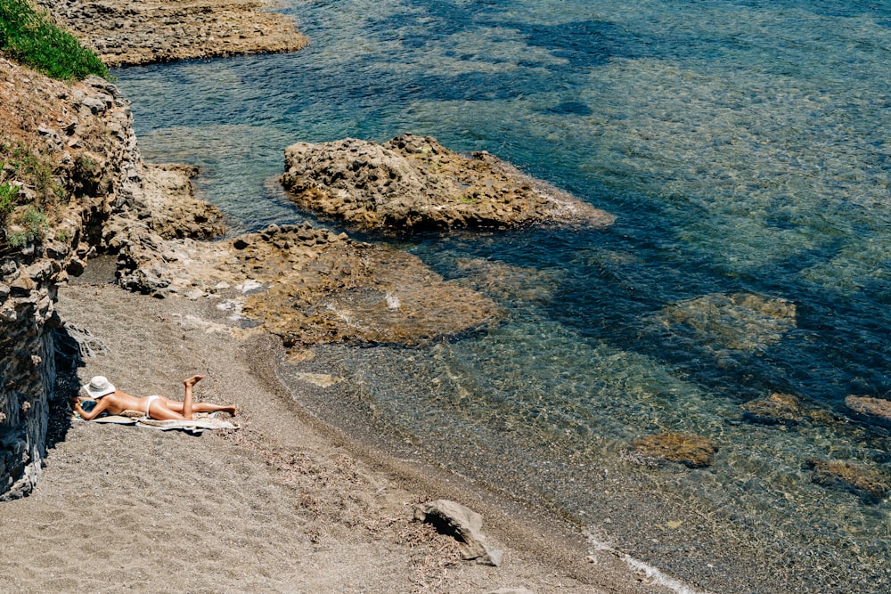 Frau im weißen Bikini liegt tagsüber am grauen Felsufer