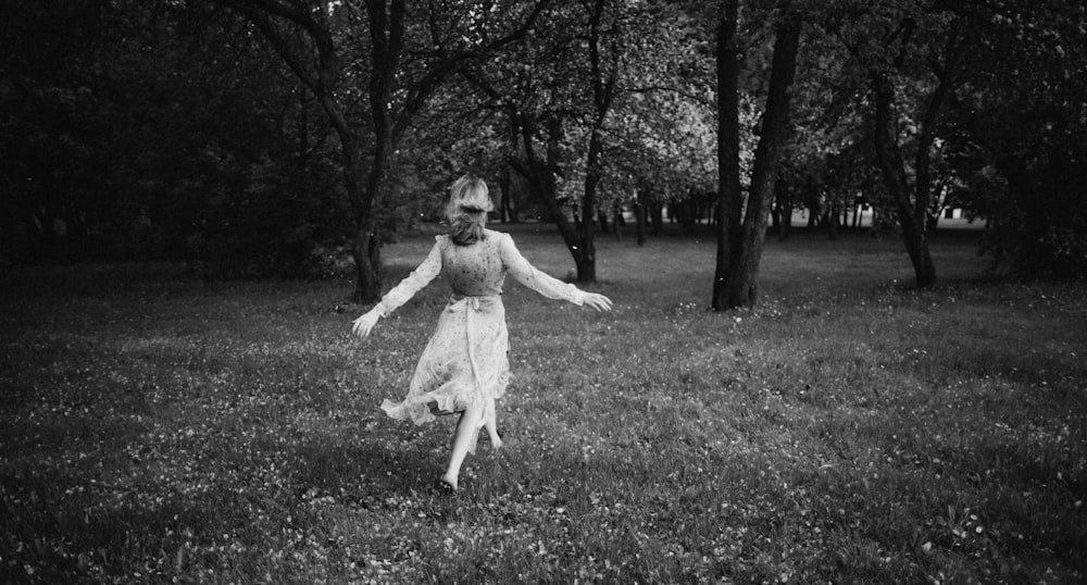 Foto en escala de grises de una chica con vestido blanco de pie en un campo de hierba