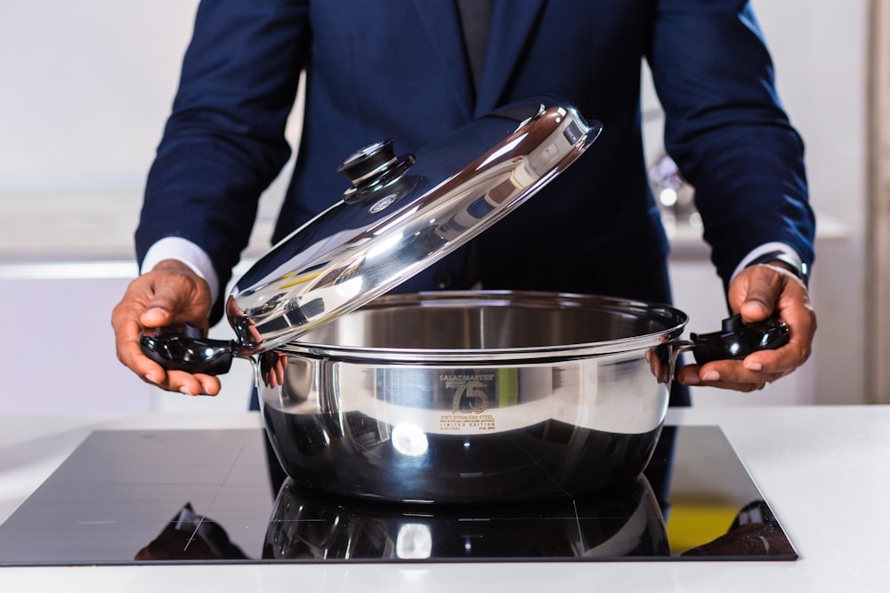 person in blue blazer holding stainless steel cooking pot